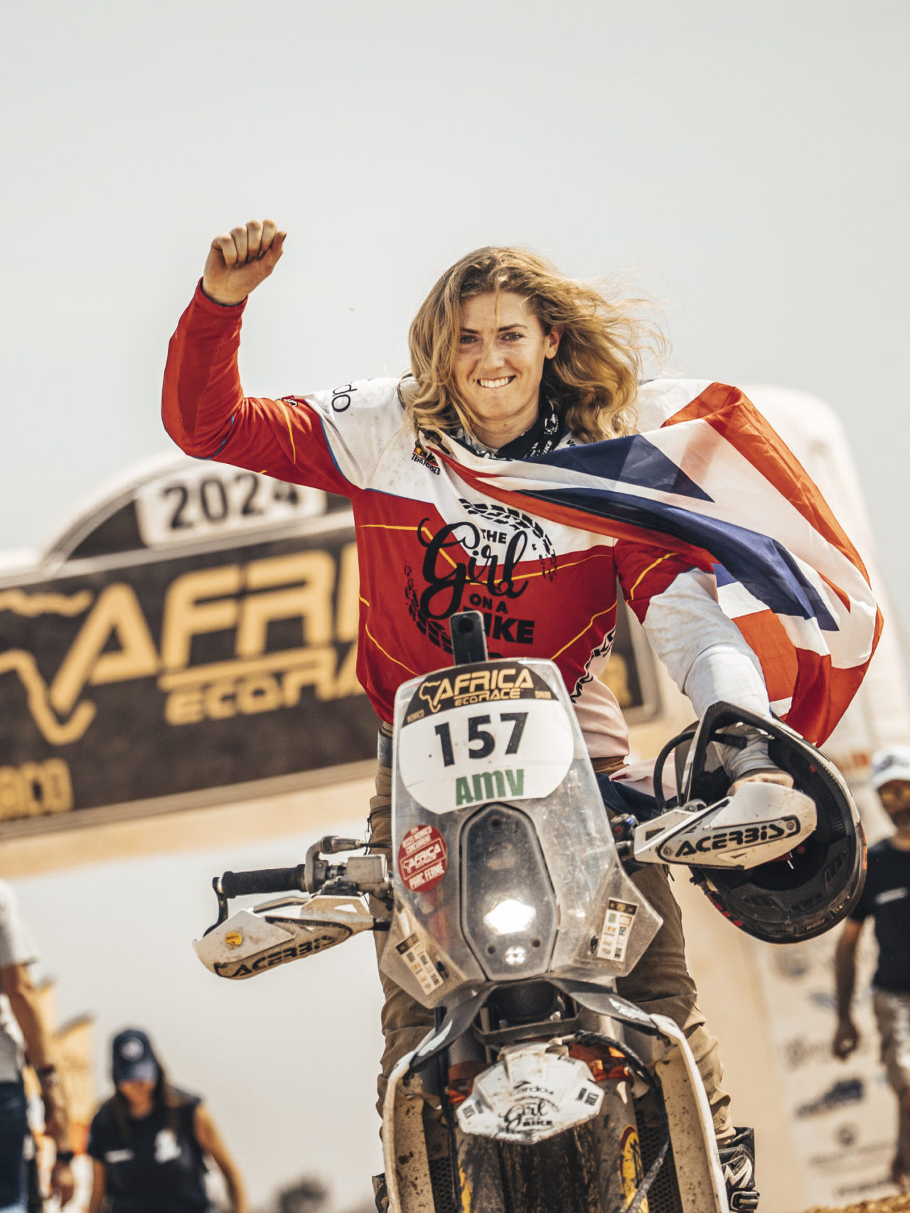 Vanessa Ruck completing the Africa Eco Race Dakar on her motorcycle, celebrating at the finish line with a flag as a result of her endurance racing achievement. Winning the female category