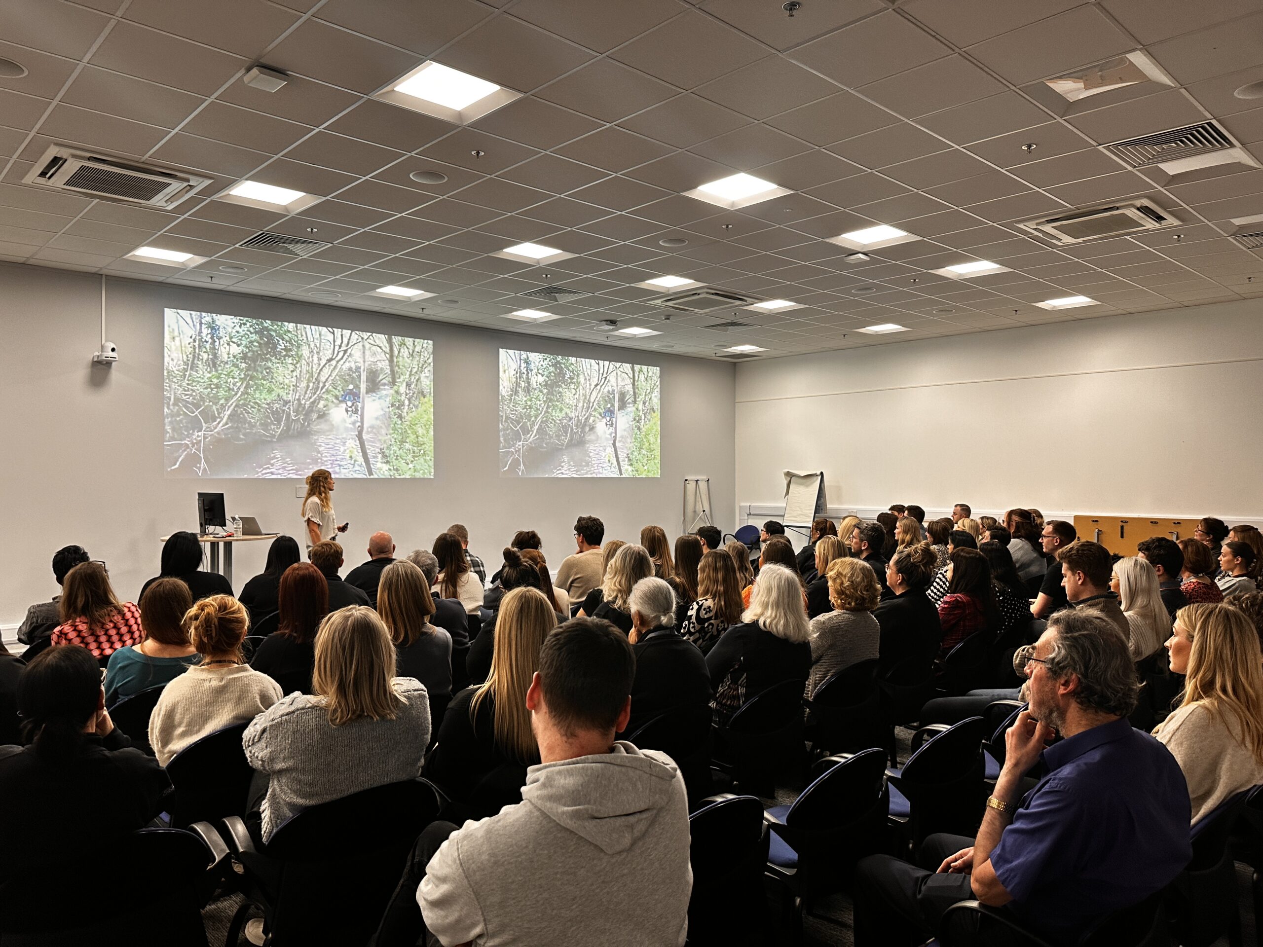 Vanessa Ruck delivering a corporate keynote on resilience and overcoming adversity to a full audience in a lecture-style conference room.