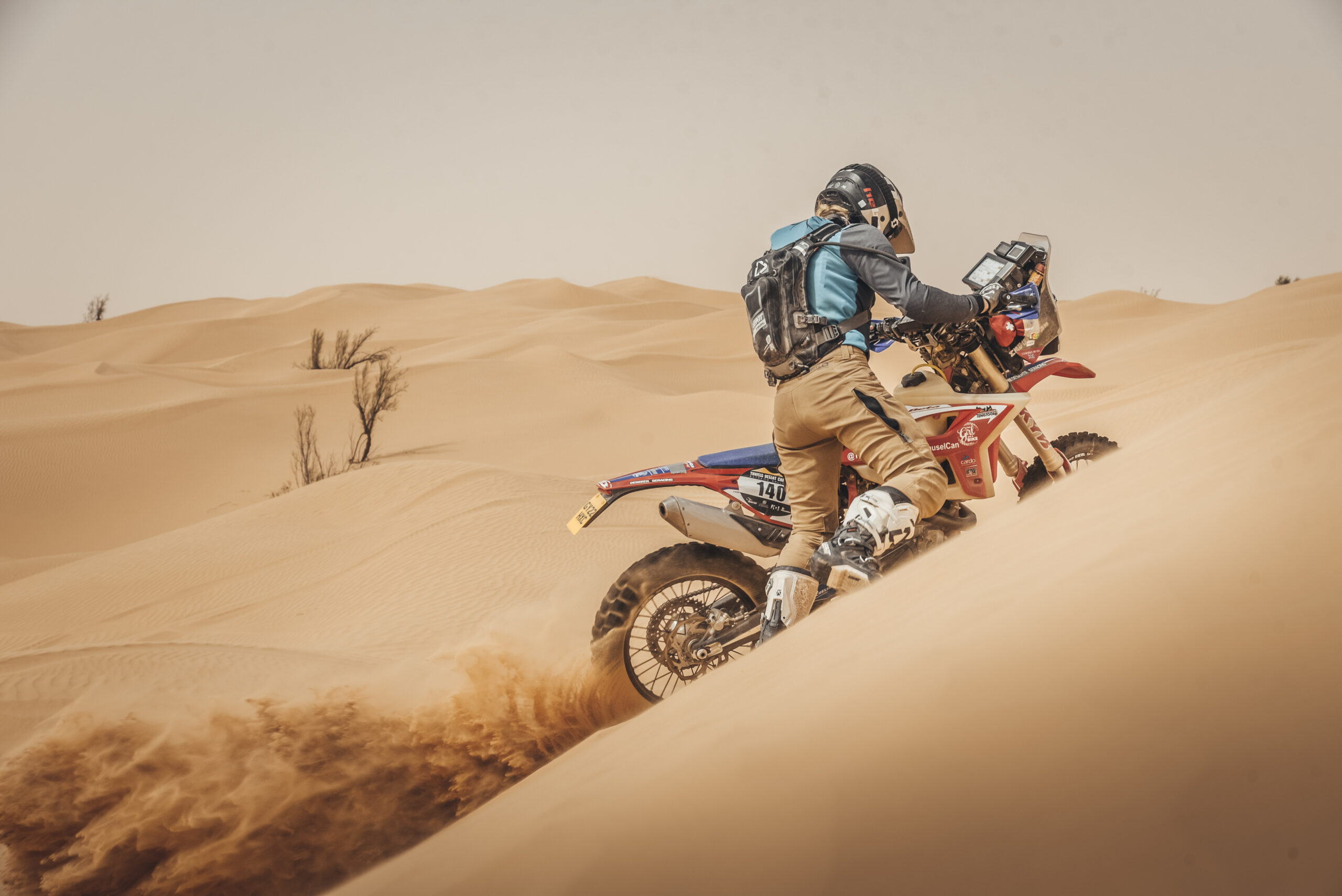 Vanessa Ruck during the Tunisia Desert Rally pushing her Beta rally bike in deep sand on a huge dune. Sand is flying out behind the spinning rear tyre